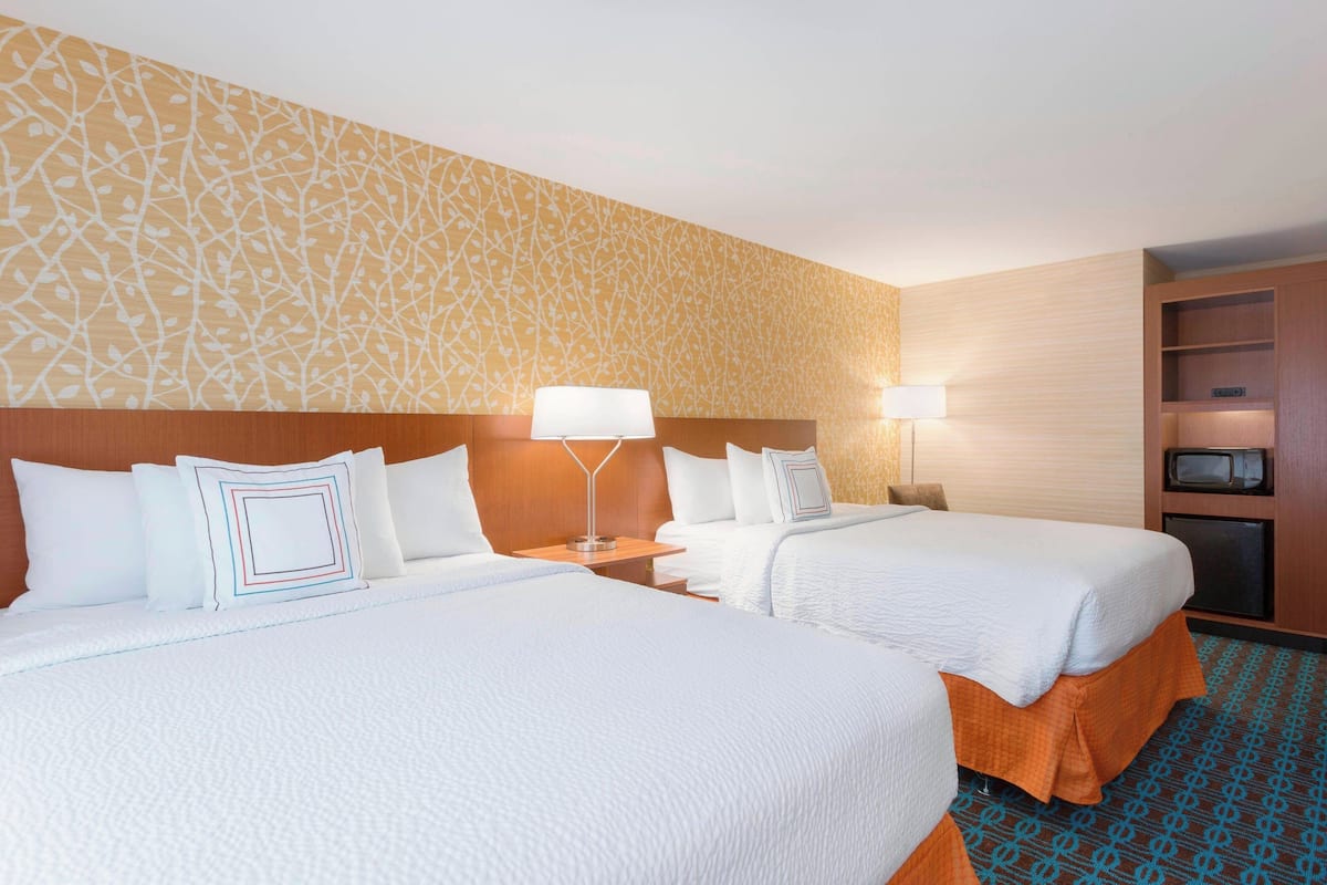 A hotel room with two beds, a wooden headboard, a patterned wall, a television, and a small shelf.