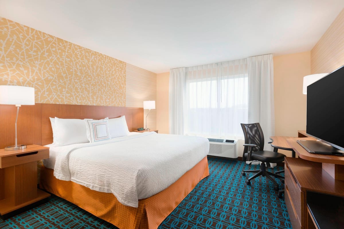 A hotel room with a large bed, a desk with a computer, a chair, a TV, and a window with curtains.