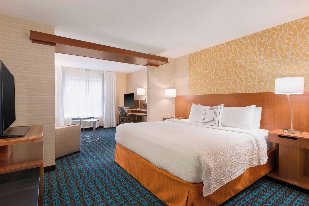 A hotel room with a large bed, a desk, and a TV.