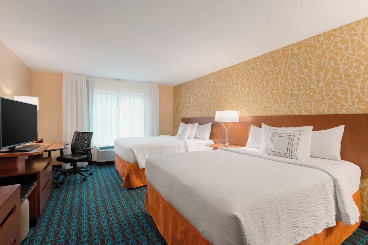 A hotel room with two beds, a desk with a computer, a TV, and a chair.