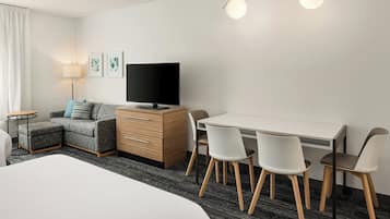Una habitación de hotel moderna con una cama, un sofá, un escritorio con sillas, un televisor y una lámpara.