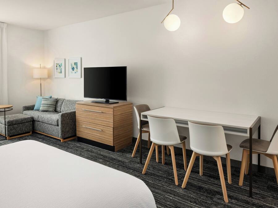 Una habitación de hotel moderna con una cama, un sofá, un escritorio con sillas, un televisor y una lámpara.