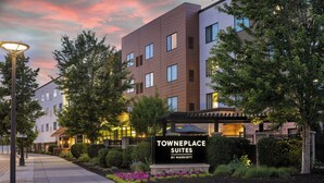 Un hotel moderno con un letrero que dice 'Towneplace Suites by Marriott', rodeado de jardines ajardinados y árboles.