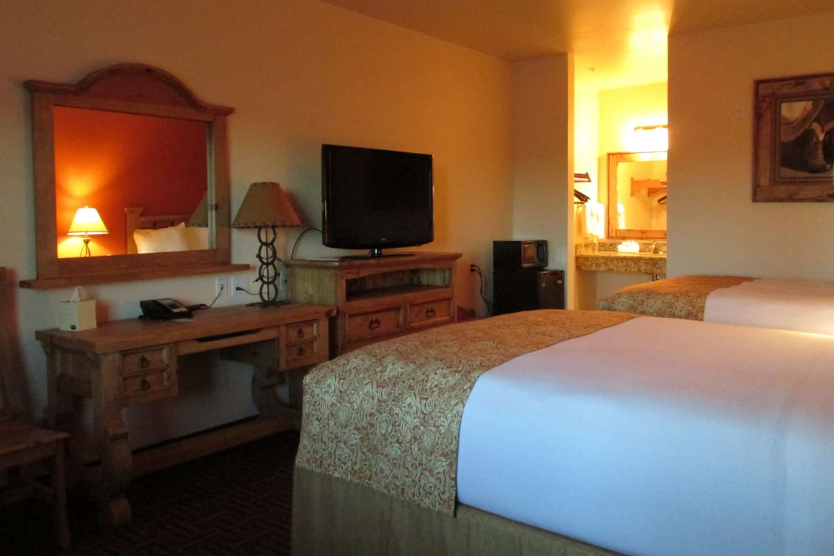 Ein Hotelzimmer mit Bett, Fernseher, Schreibtisch mit Schubladen, Lampe und Spiegel.