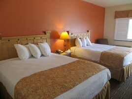 Una habitación de hotel con dos camas, una mesita de noche con lámpara y una ventana con persianas.