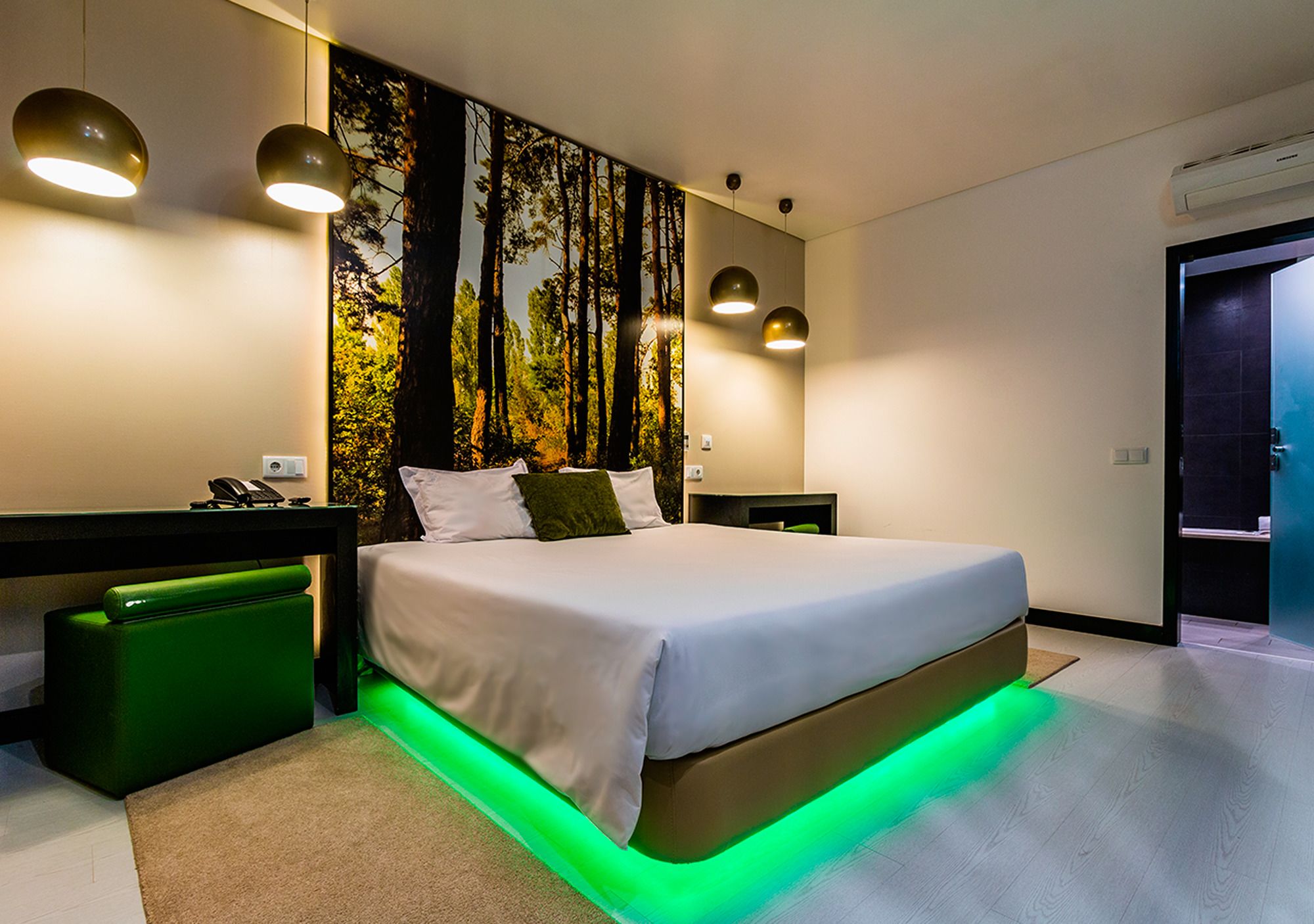 A modern bedroom with a large bed, green accent lighting, and a forest-themed wall mural.
