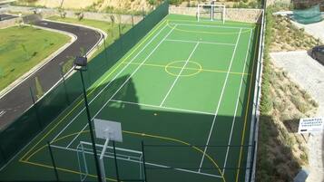 A tennis court with a net, surrounded by a fence, and a road nearby.
