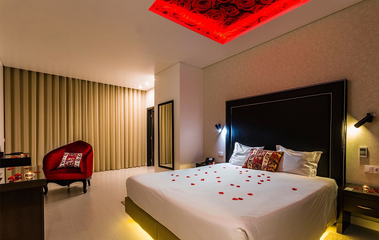 A hotel room with a large bed, a red armchair, a desk with a lamp, and a ceiling light fixture.