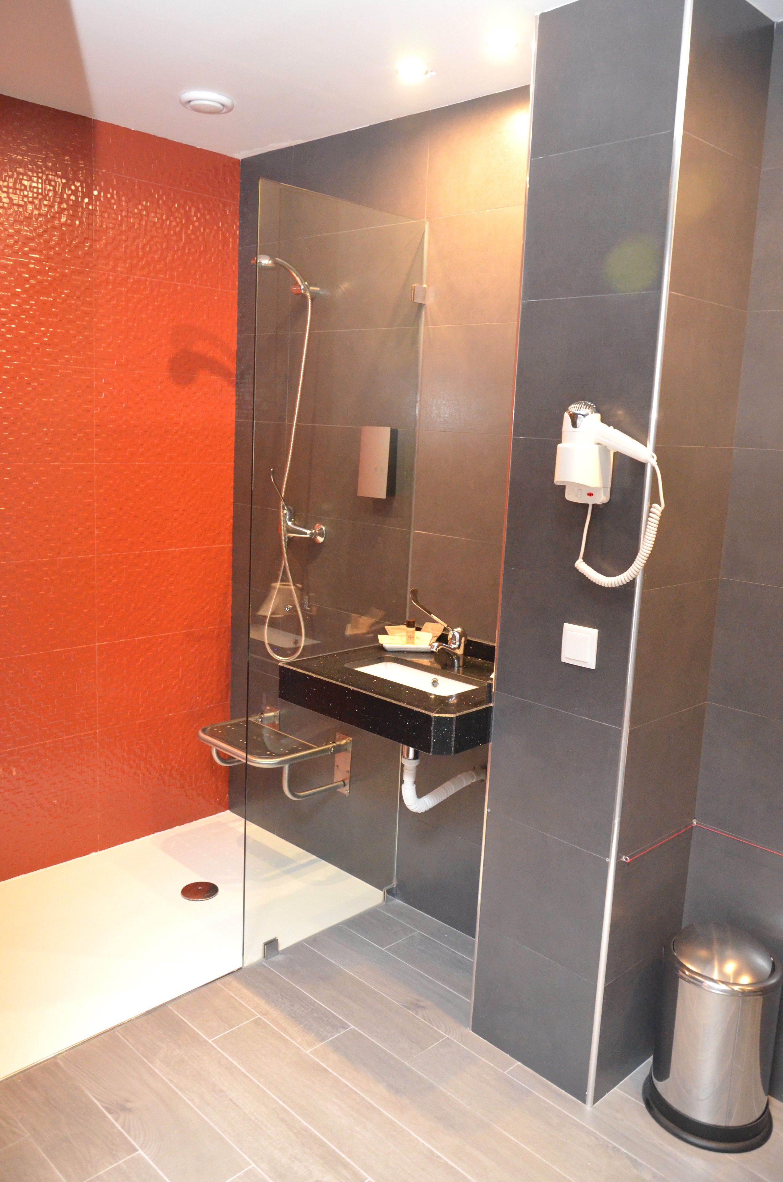A modern bathroom with a glass-enclosed shower, a vanity with a sink, and a hairdryer mounted on the wall.