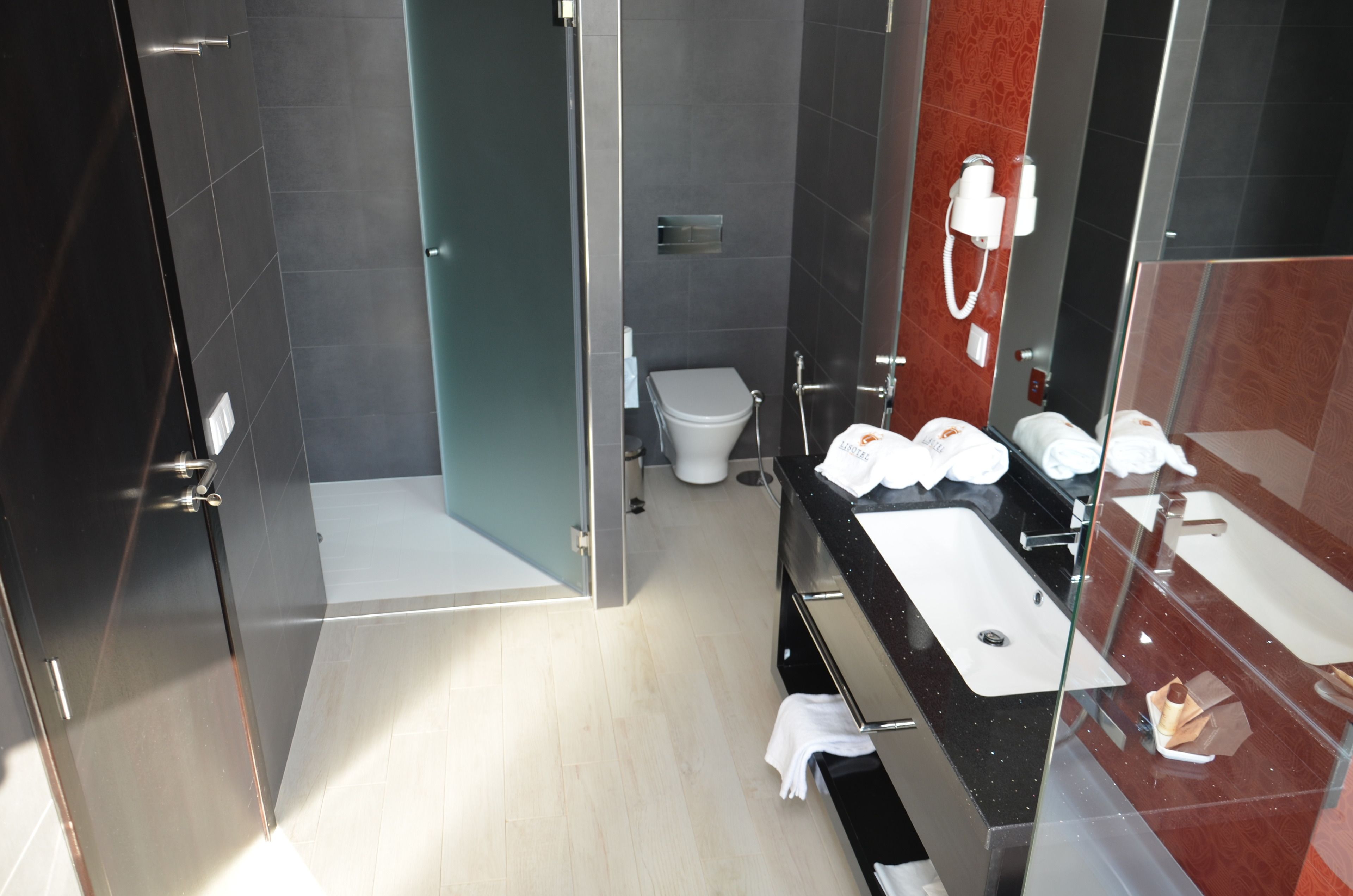 Een moderne badkamer met een douchecabine van glas, een wit toilet en een zwart badkamermeubel met twee wasbakken.