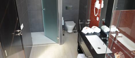 Een moderne badkamer met een douchecabine van glas, een wit toilet en een zwart badkamermeubel met twee wasbakken.