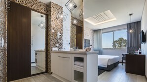 A modern hotel room with a large mirror, a bed, a desk, and a view of the outdoors.