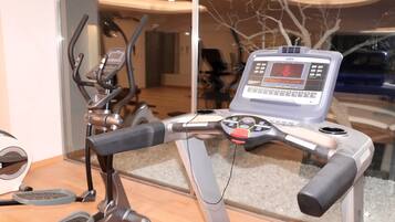 Un vélo d’appartement doté d’un écran numérique et d’un panneau de commande, placé dans une pièce dont un mur est en verre et qui offre une vue sur un arbre à l’extérieur.