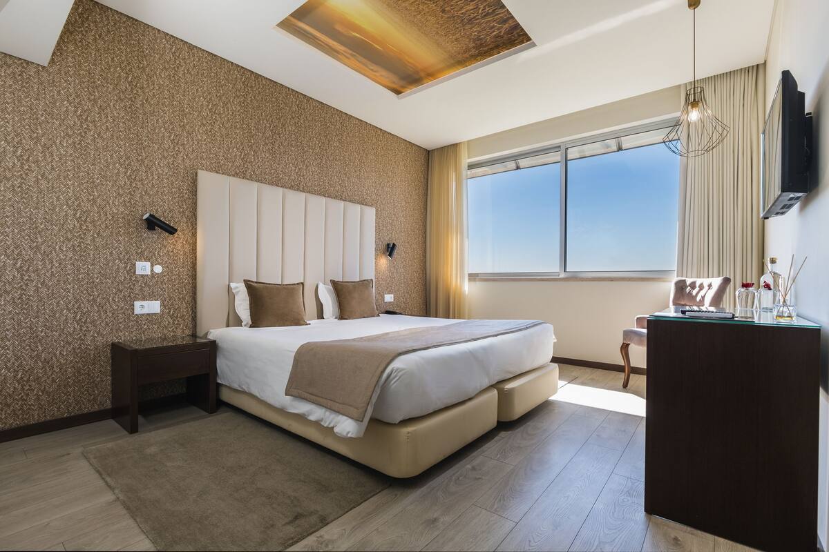 Un dormitorio moderno con una cama grande, un escritorio y un ventanal amplio.