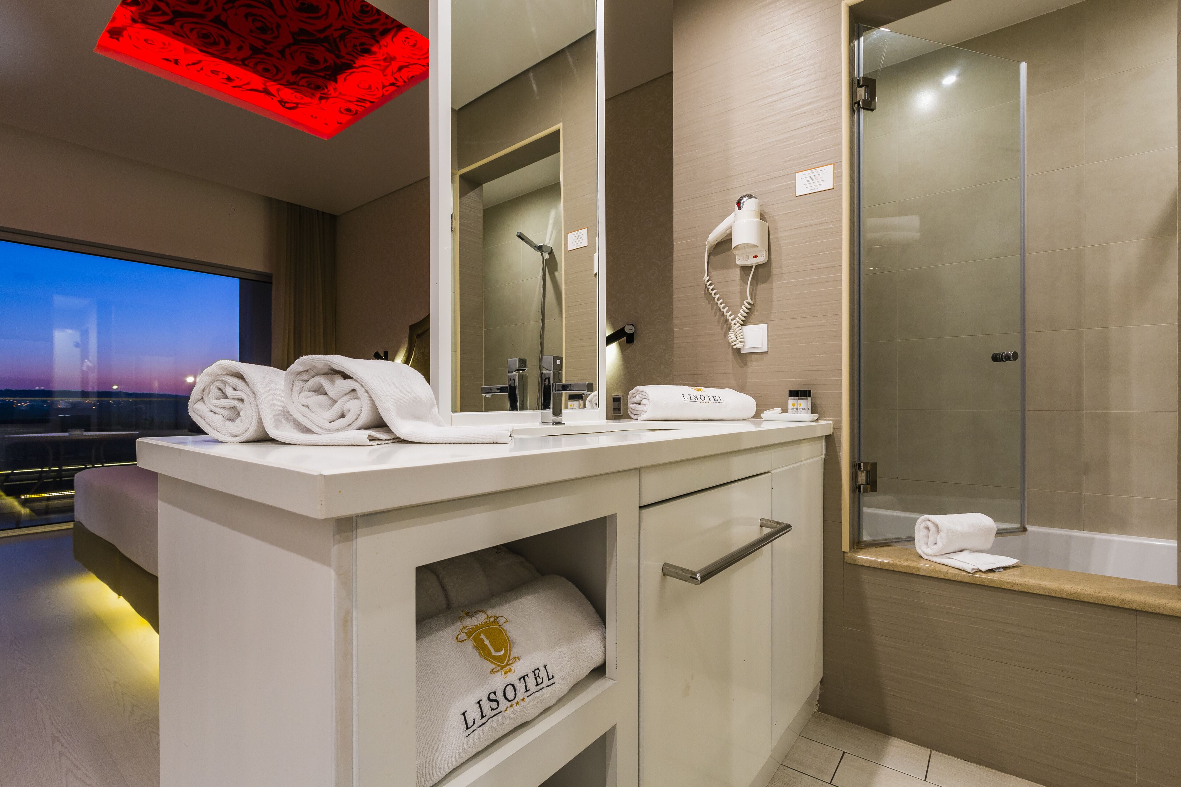 A modern bathroom with a vanity, towel storage, a hairdryer, and a glass-enclosed shower.
