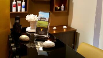 A hotel reception area with a black reception desk, a telephone, a brochure stand, and shelves with toiletries.