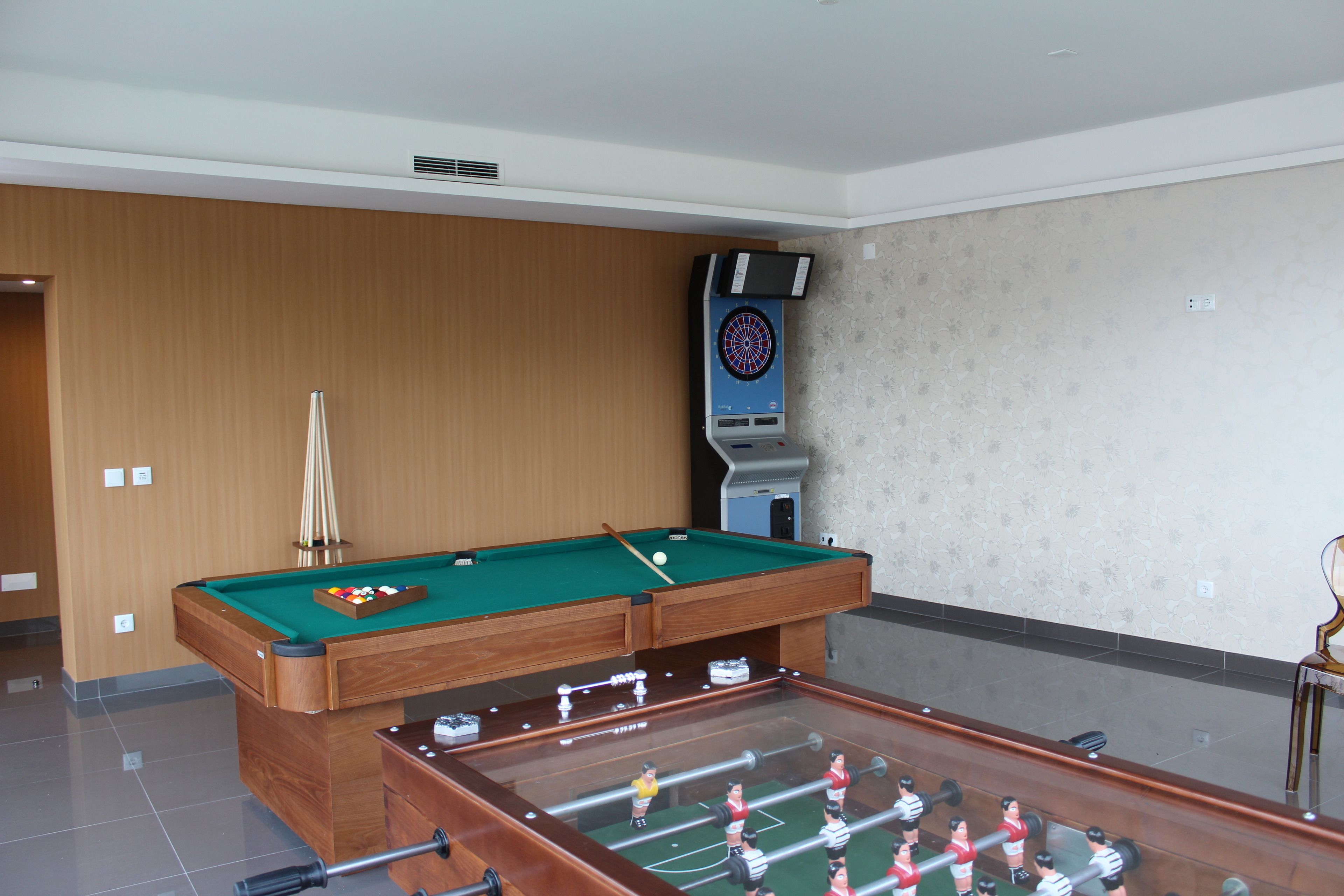 Una mesa de billar junto a una mesa de fútbolín en una sala con paneles de madera y un dardo.