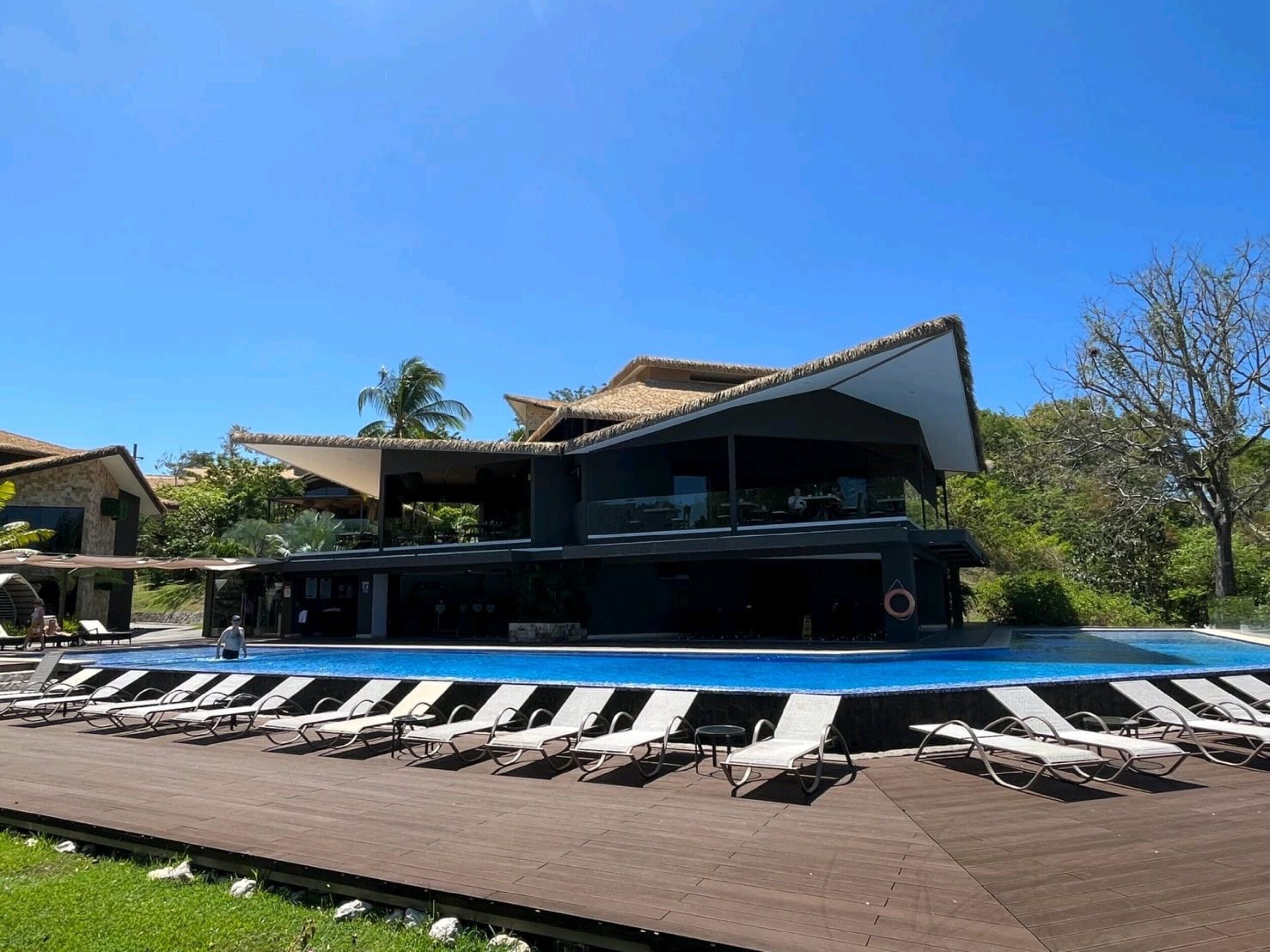 A modern building with a pool area, including lounge chairs and a dining area.