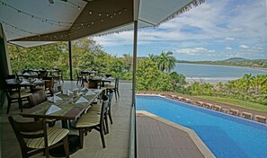 An outdoor dining area with tables and chairs, overlooking a pool and a beach. - Nammbú Beachfront Bungalows (Puerto Carrillo)