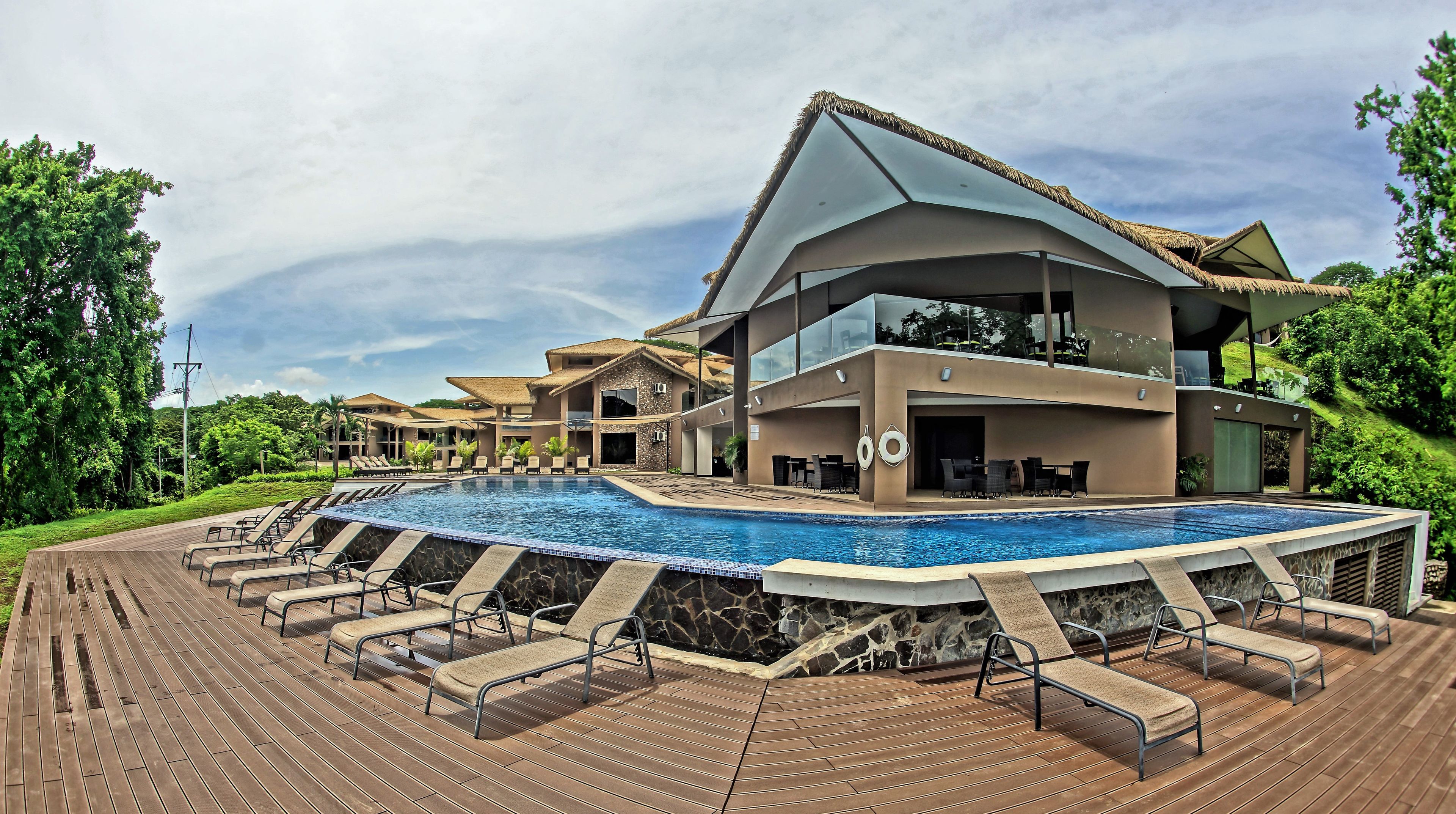 A resort with a swimming pool, lounge chairs, and a modern building with a thatched roof.