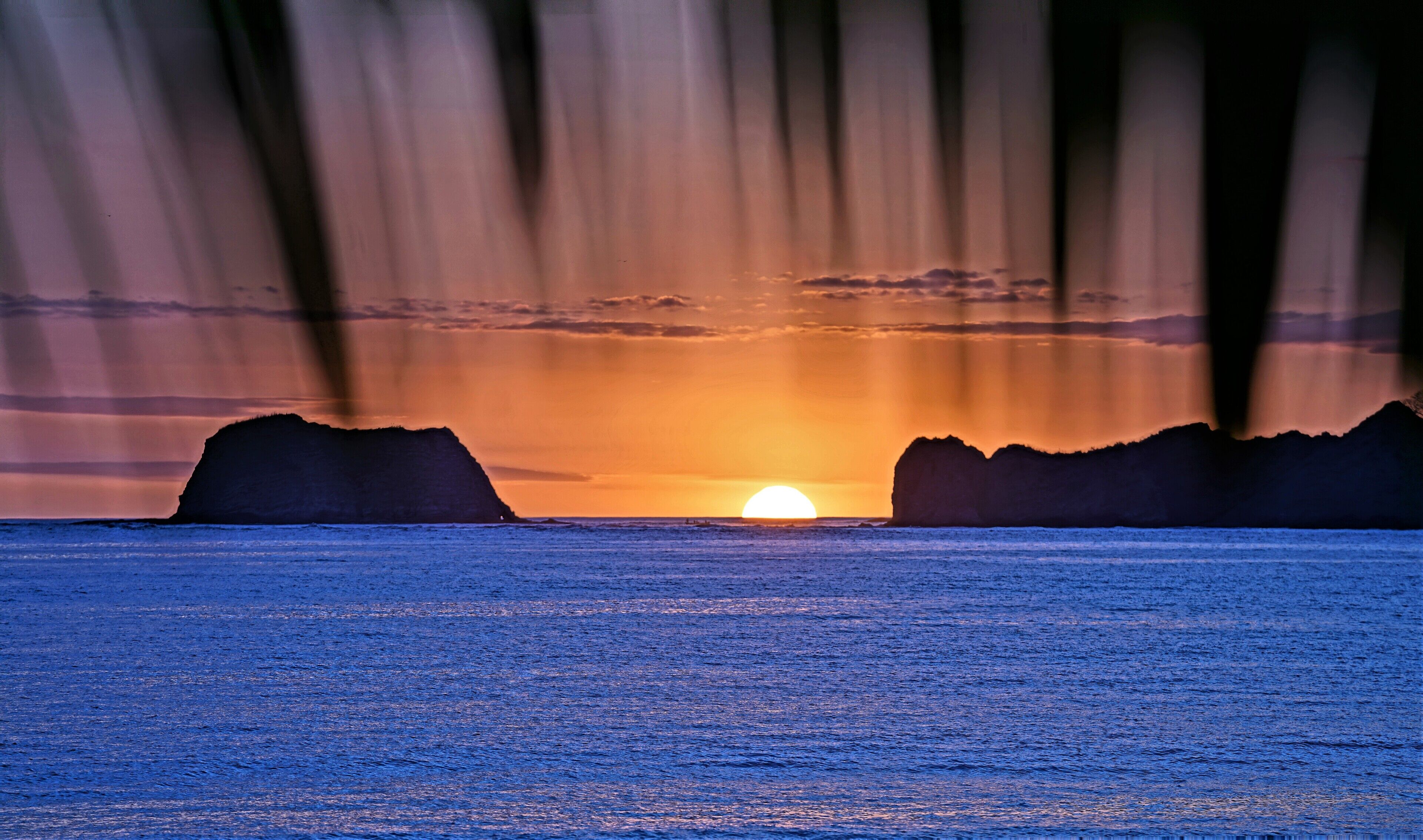 A sunset over a calm sea with two prominent rock formations on either side.