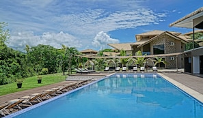 A swimming pool with lounge chairs, a covered seating area, and a building with a thatched roof. - Nammbú Beachfront Bungalows (Puerto Carrillo)