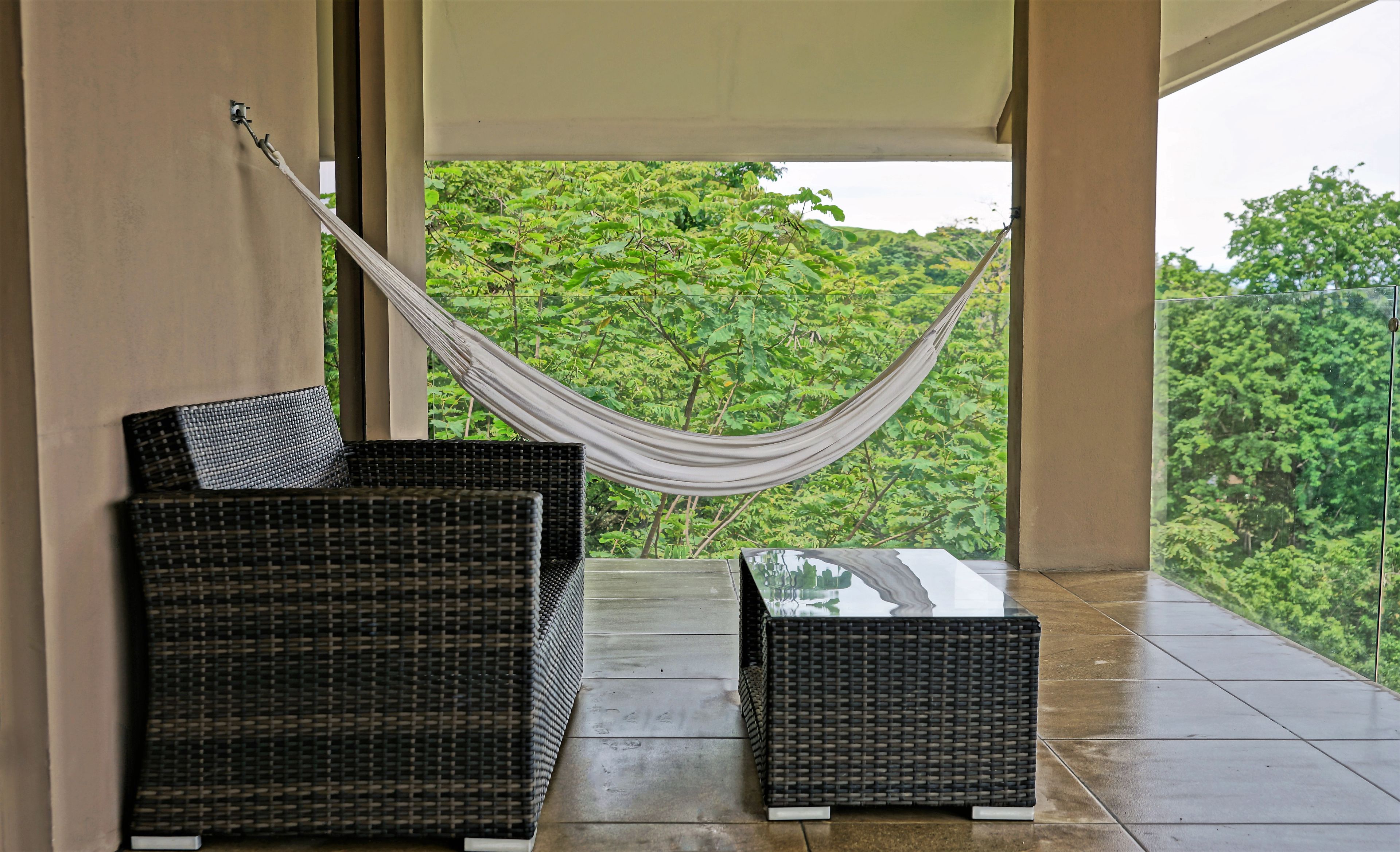 A balcony with wicker furniture, a hammock, and a view of lush greenery.