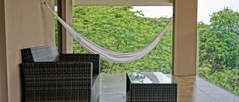 A balcony with wicker furniture, a hammock, and a view of lush greenery.