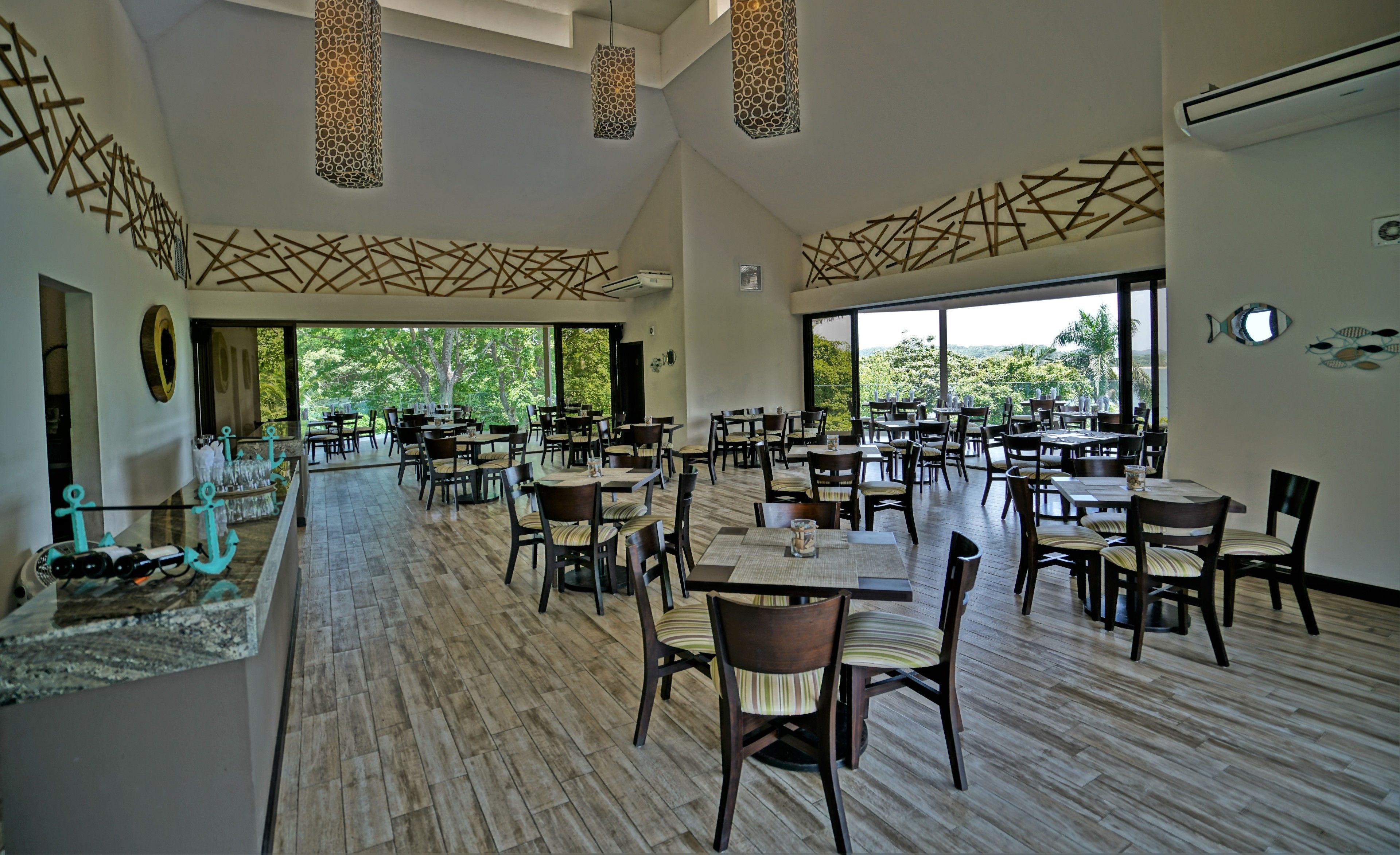 A spacious dining area with multiple tables and chairs, large windows offering a view of the outdoors, and decorative wall art.