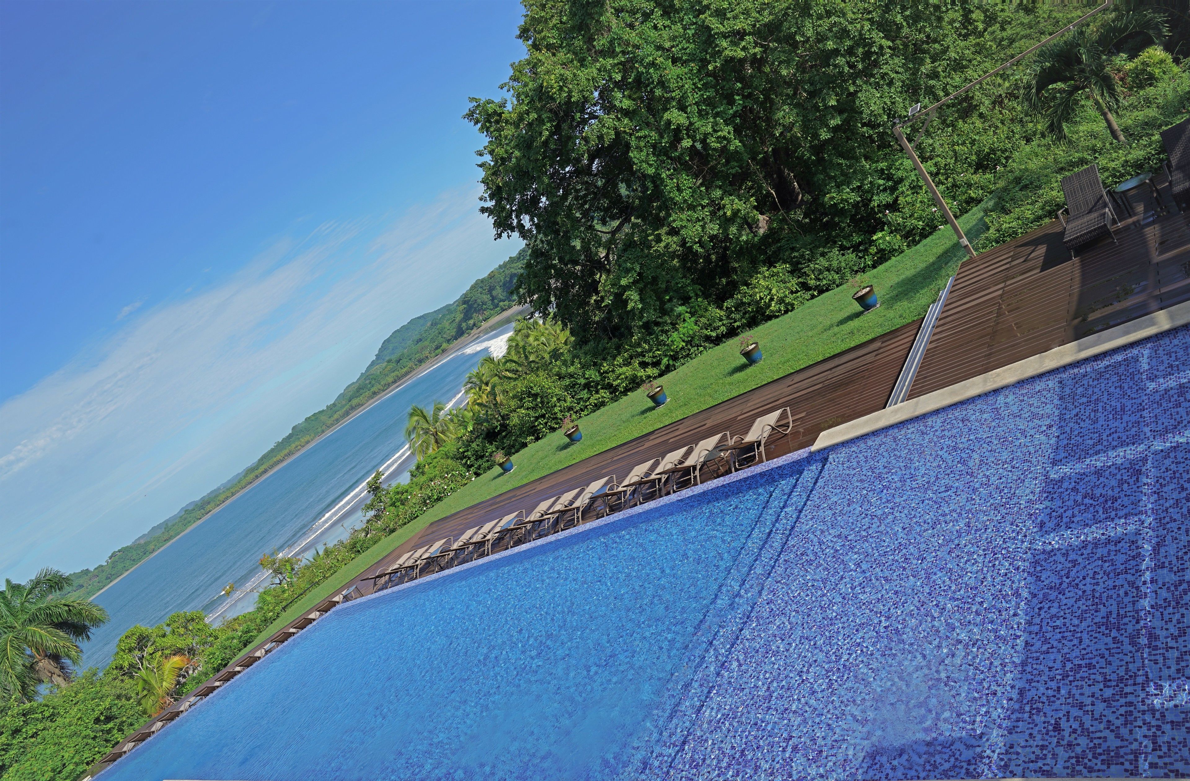 A swimming pool with a view of the ocean, surrounded by greenery and lounge chairs.