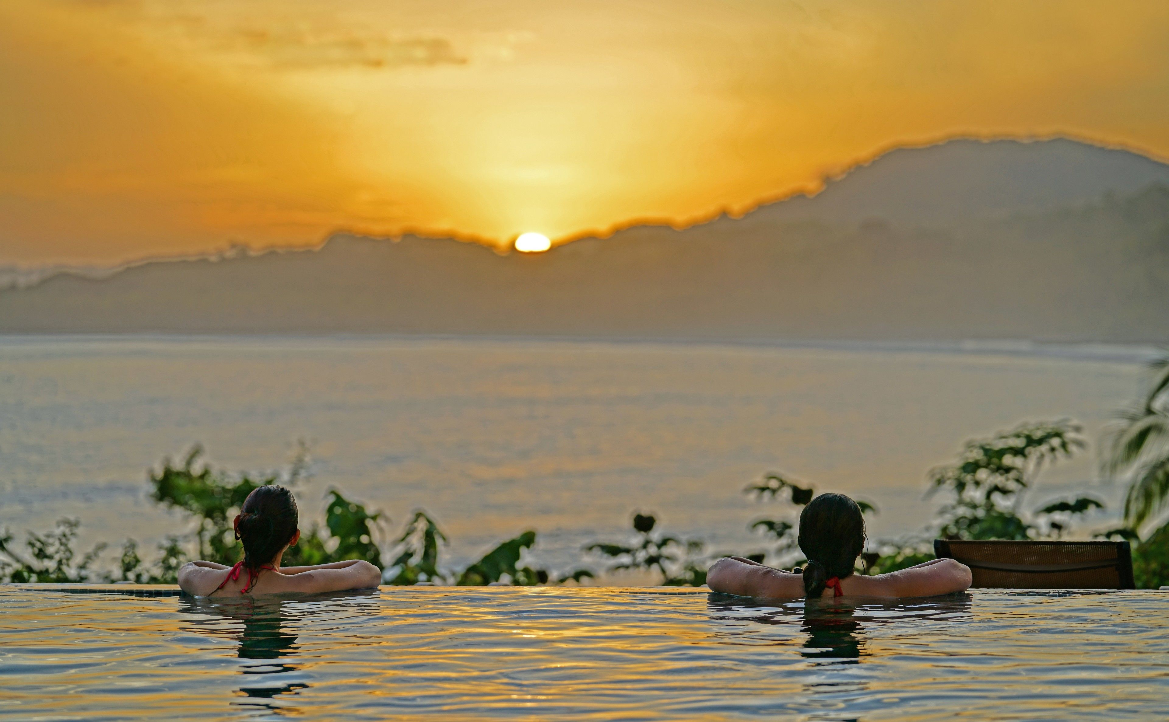 Dos personas descansando en una piscina con vistas al atardecer.