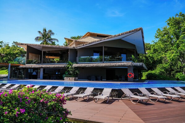 Un moderno resort con piscina, sillones de descanso y una estructura de techo de paja.