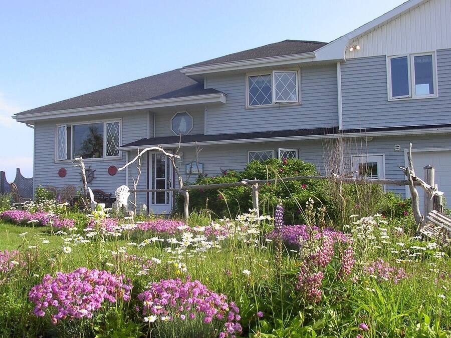 A two-story house with a front porch, a small garden with various flowers, and a wooden fence.