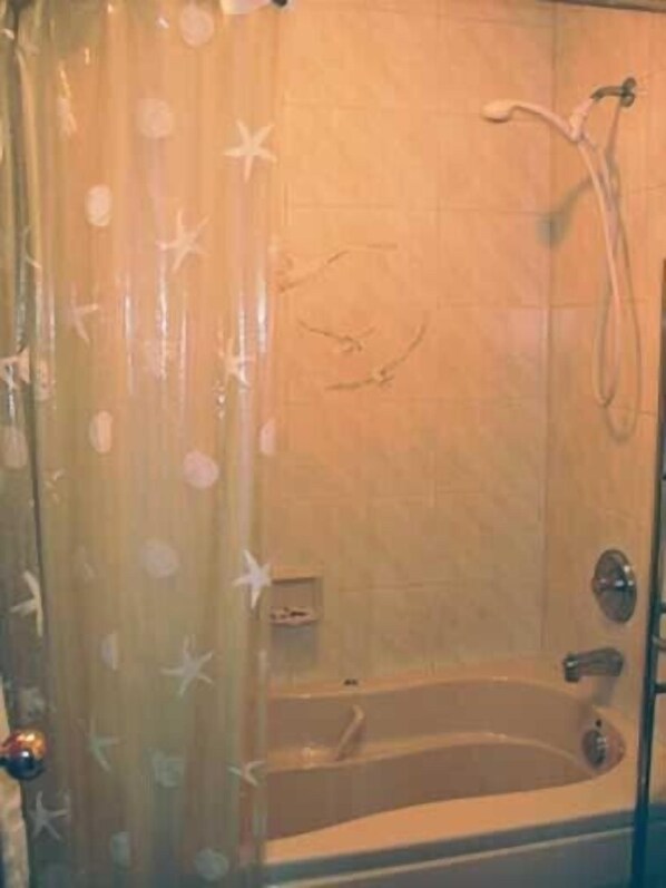 Un baño con bañera, ducha y cortina decorada con estrellas de mar.