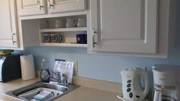 A kitchen with white cabinets, a sink with a dish rack, a coffee maker, and a kettle.