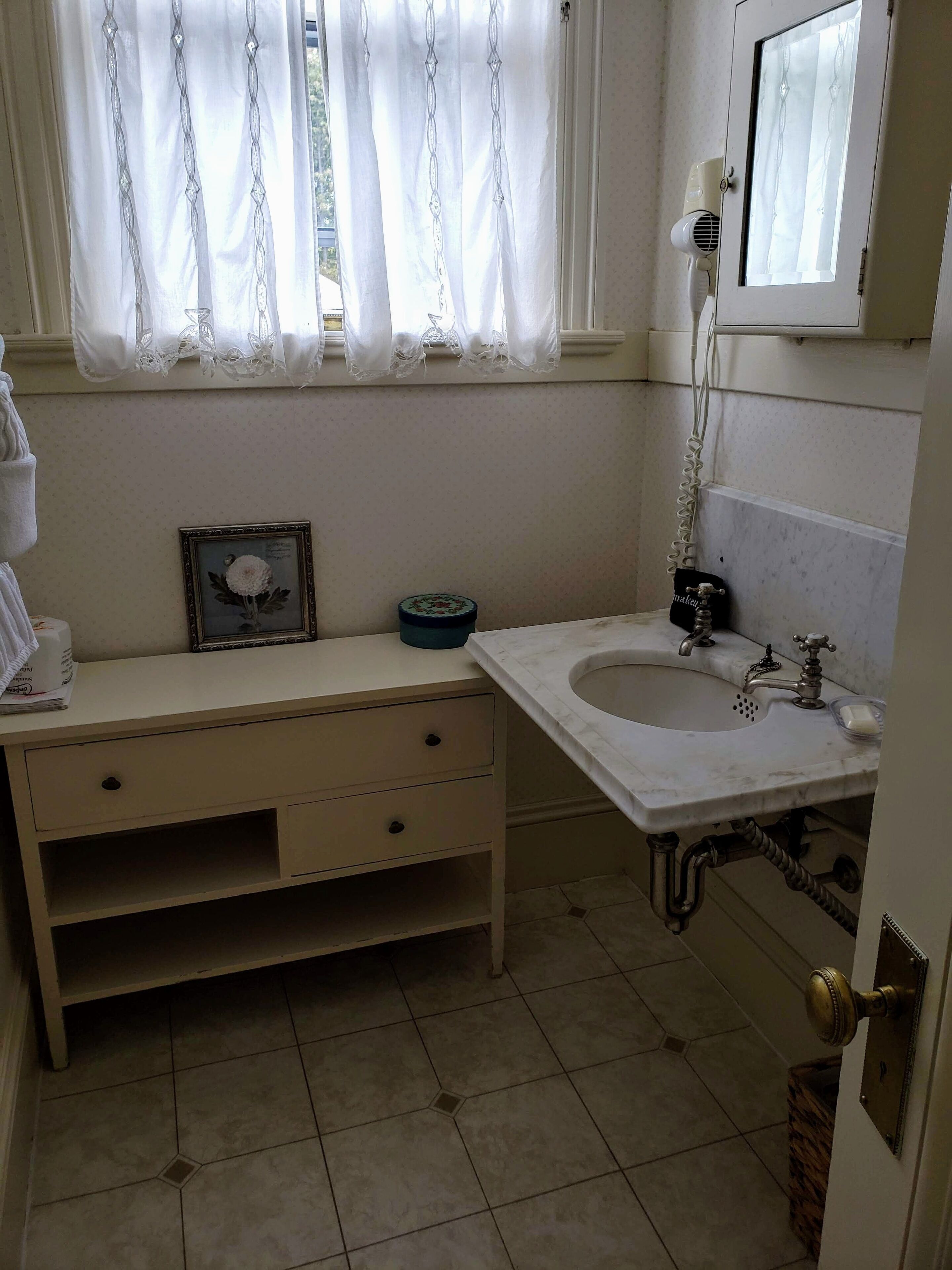 A bathroom with a white sink, a mirror, a towel rack, and a framed picture on the vanity.