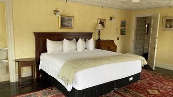A hotel room with a large bed, a wooden headboard, a bedside table, a nightstand, a lamp, a ceiling fan, and a red patterned rug.