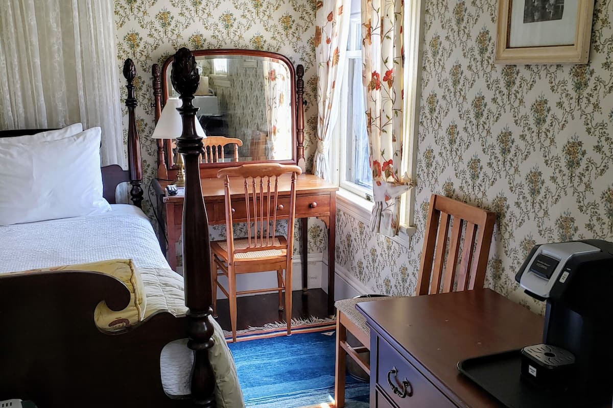 A bedroom with a bed, a desk, a chair, a dresser, and a coffee maker.