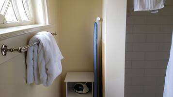 A bathroom with a window, a towel rack, a small shelf with a hairdryer, and a shower area.