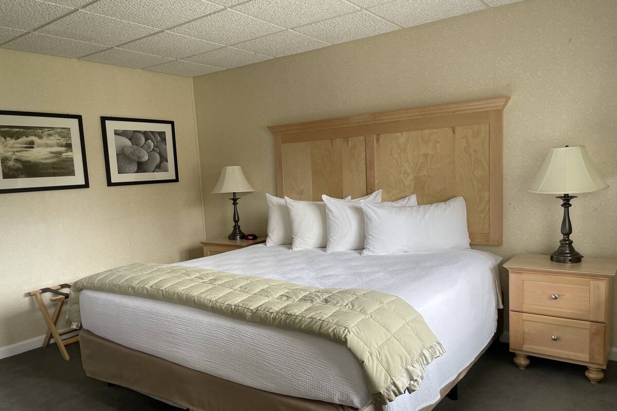 A neatly made bed with a beige quilt, two bedside tables with lamps, and two framed pictures on the wall.