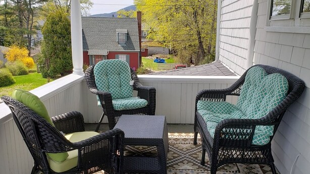 A covered porch with wicker furniture and a patterned rug.