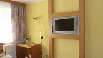 A hotel room with a bed, a desk, a chair, a television mounted on the wall, and a window with curtains.