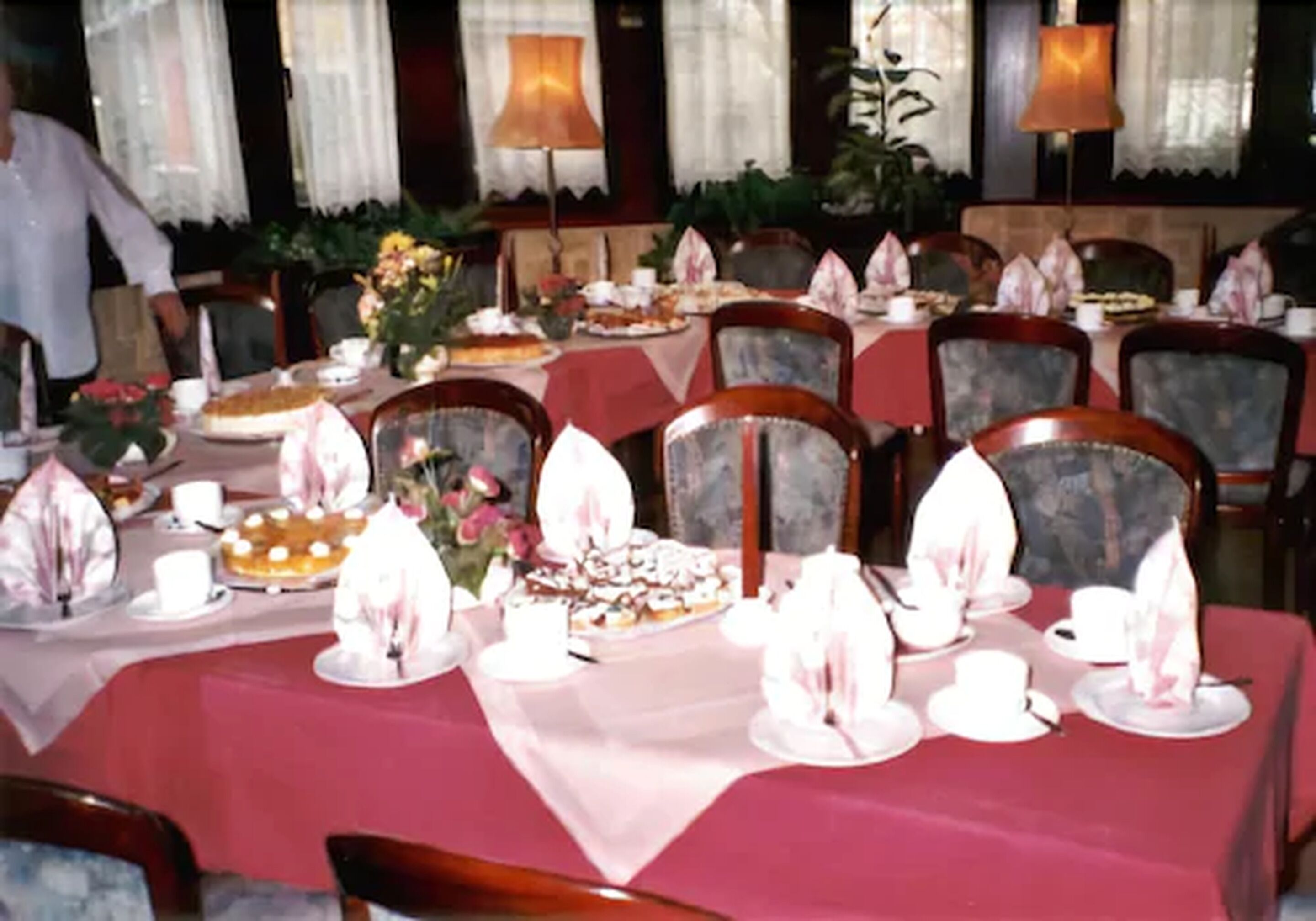 A dining area with tables set for multiple guests, each with a red tablecloth, white napkins, and various dishes.