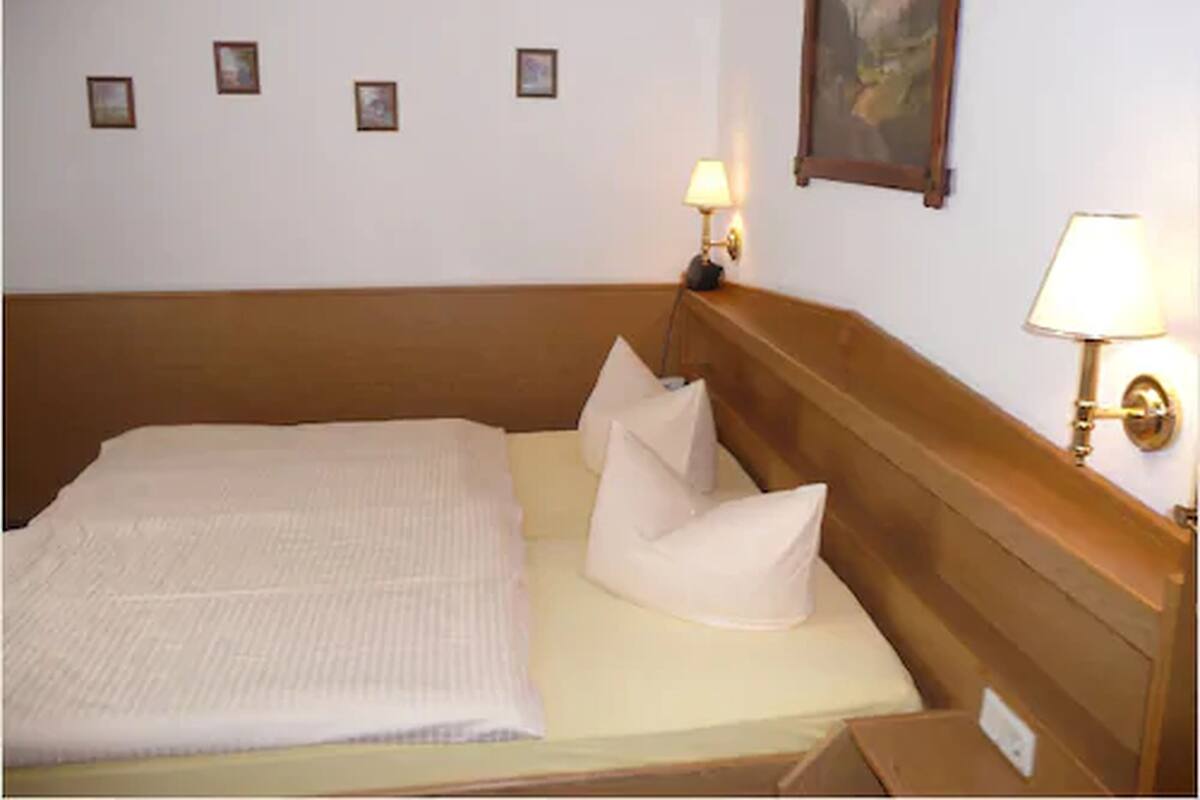 Ein ordentlich bezogenes Bett mit einem hölzernen Kopfteil, einem Bild an der Wand und zwei Wandleuchten.