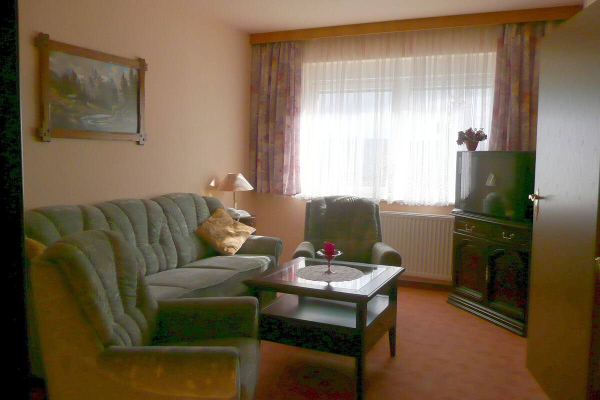 Ein Wohnzimmer mit Sofa, Sessel, Couchtisch und einem Fernseher auf einem Schrank.