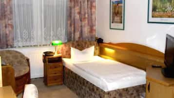 Ein Hotelzimmer mit einem Bett, einem Schreibtisch, einem Sessel, einem Nachttisch mit Lampe und einem Fernseher.