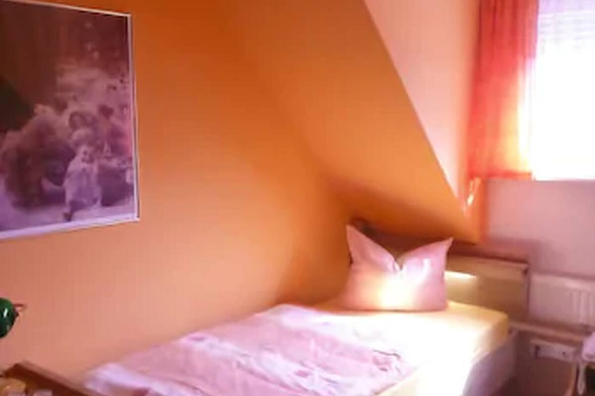 Ein Schlafzimmer mit einem Bett, einem Nachttisch, einem Heizkörper und einem Fenster mit Vorhängen.