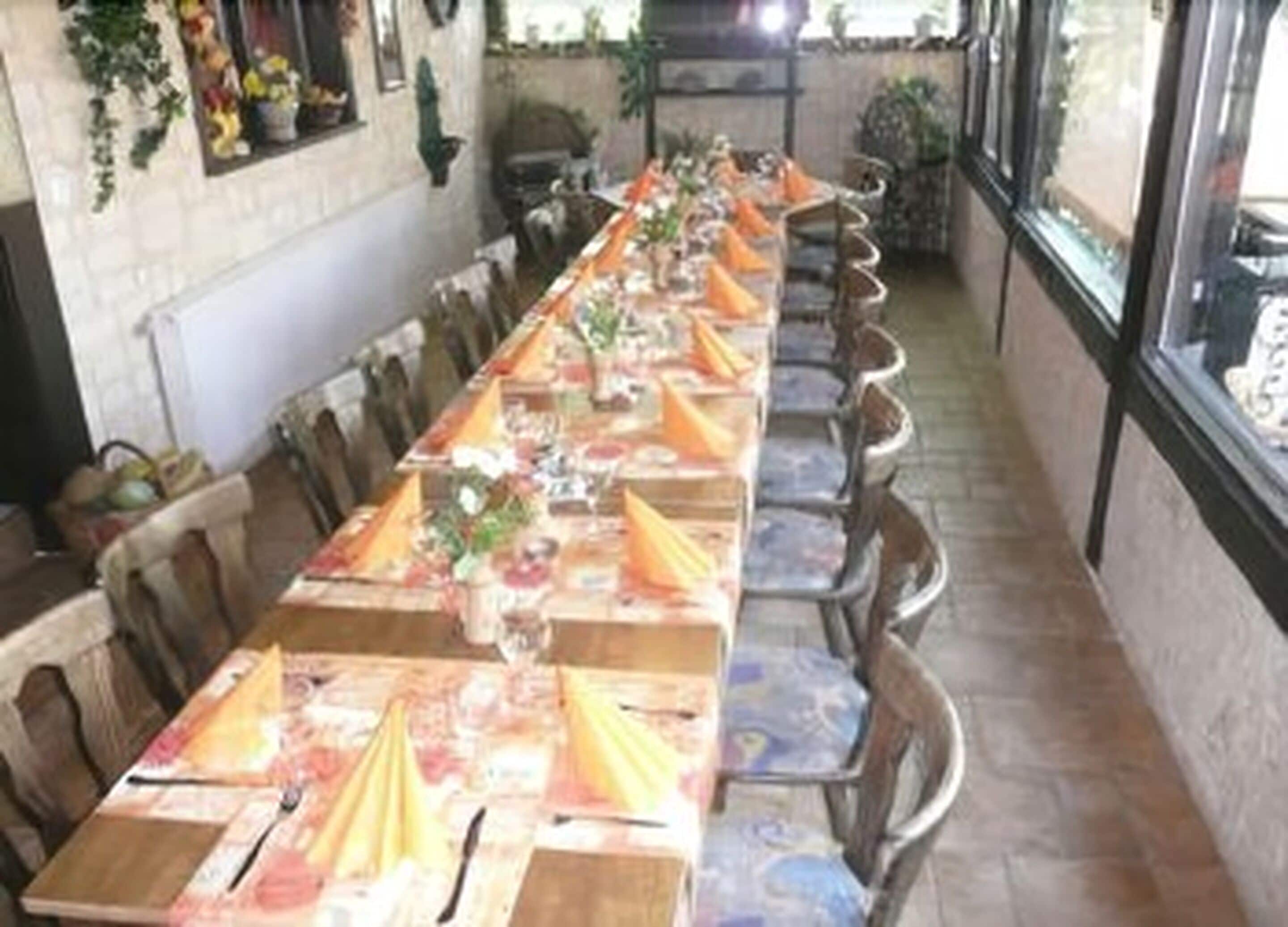 Une longue table à manger, agrémentée de chaises, décorée avec des serviettes orange et des compositions florales.