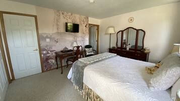 Une chambre à coucher comprenant un lit, un bureau, une chaise, une commode, un miroir et un téléviseur fixé au mur.