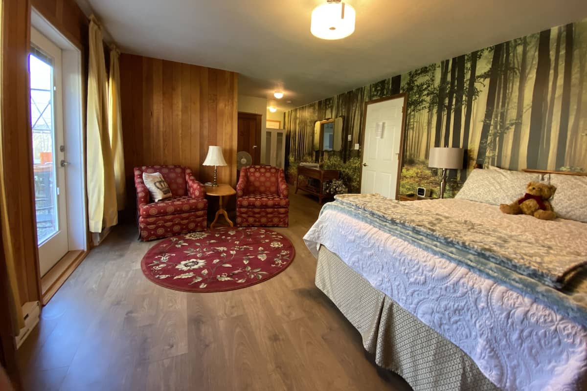 Een hotelkamer met een bed, twee fauteuils, een kleine tafel, een rood vloerkleed met bloemenmotief en een muurschildering van een bos.